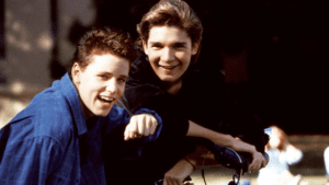 Two young men smile for the camera while sitting on a bicycle.