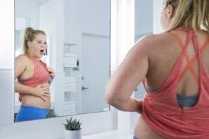 A woman looking at her stomach in the mirror.