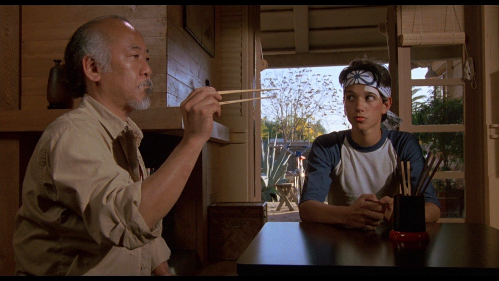 A man and boy sitting at a table with chopsticks.