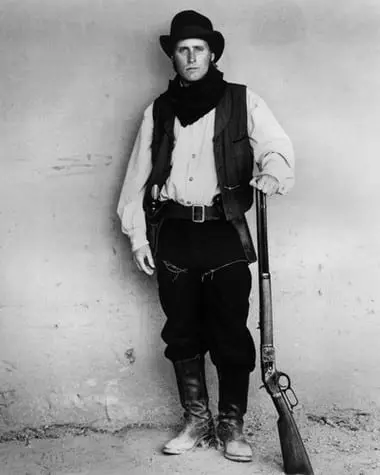 A man in black and white standing with a rifle.