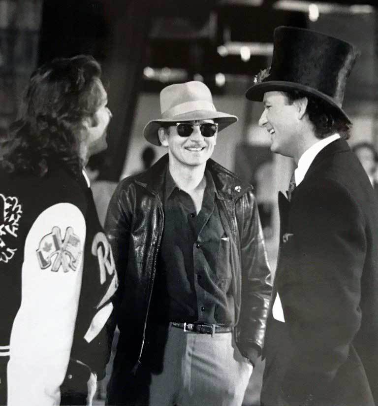 A man in top hat and sunglasses standing next to two other men.