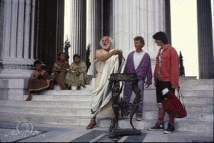 A man in toga costume standing on steps with other people.