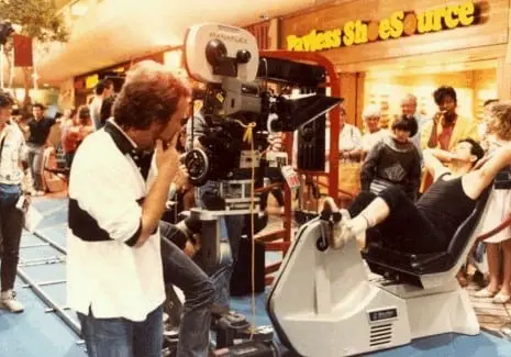 A man standing next to a camera on top of a bench.