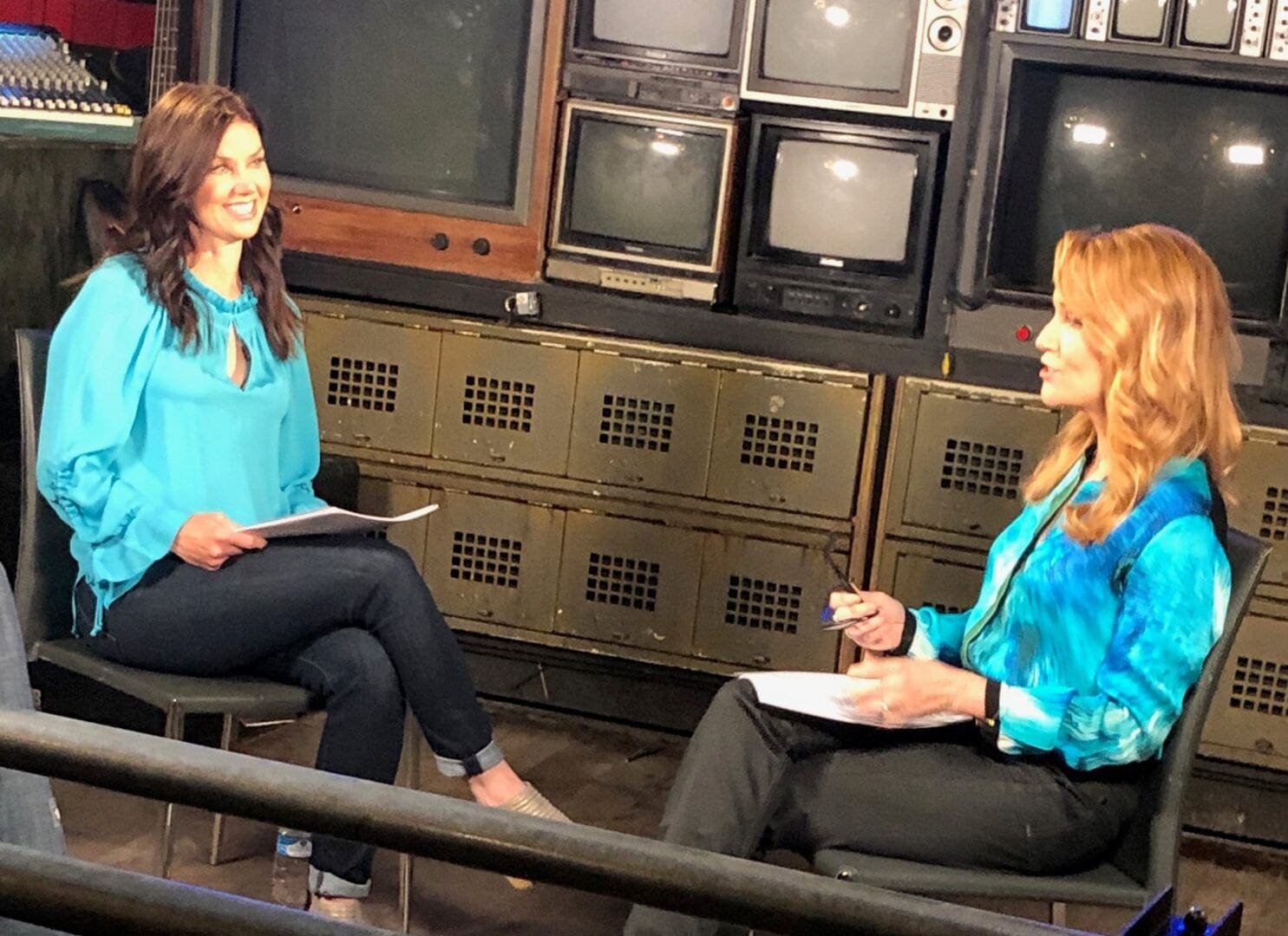 Two women sitting on a bench in front of some old tvs.