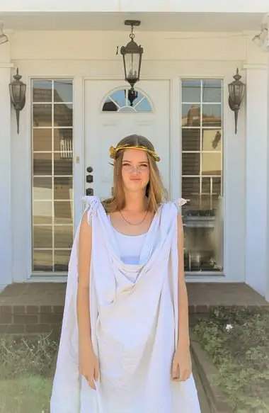 A woman in greek costume standing outside of a house.