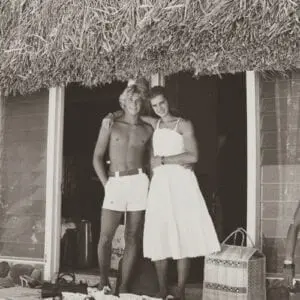 A man and woman standing in front of a hut.
