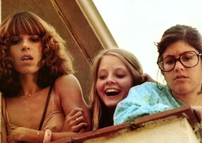 Three women are smiling while looking out a window.