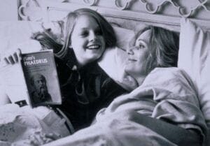 Two women laying in bed with a magazine.