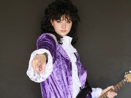 A woman in purple and white outfit pointing at the camera.