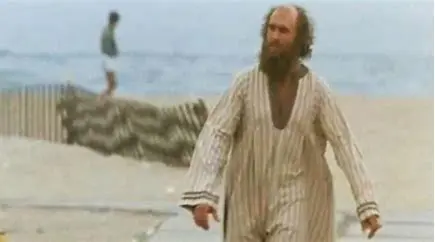 A man in striped pajamas walking on the beach.