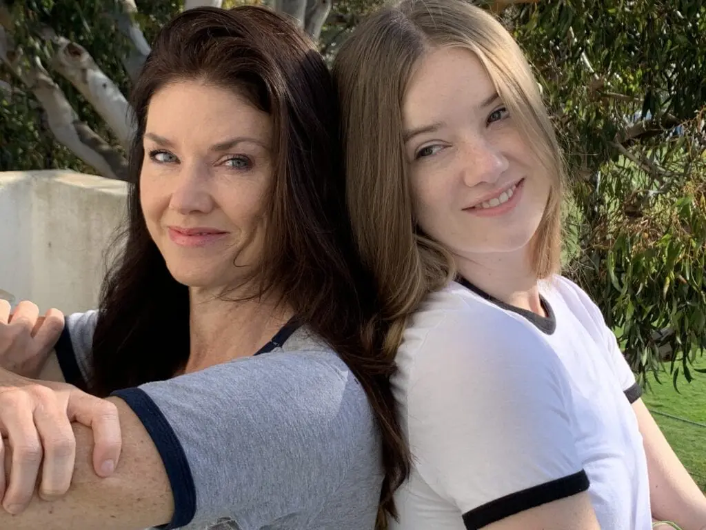 Two women standing next to each other in front of a tree.